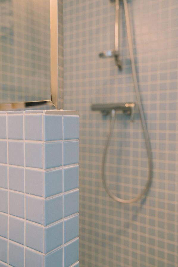 A bathroom with blue checkered tiles, a shower with a handheld hose, and a mirror above the sink. - Hotel Et Bistrot Du Bac (Combrit)