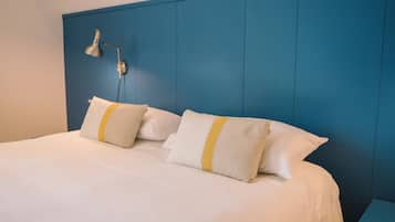 Un lit avec une literie blanche et deux oreillers, une tête de lit bleue et une table de chevet avec une lampe.