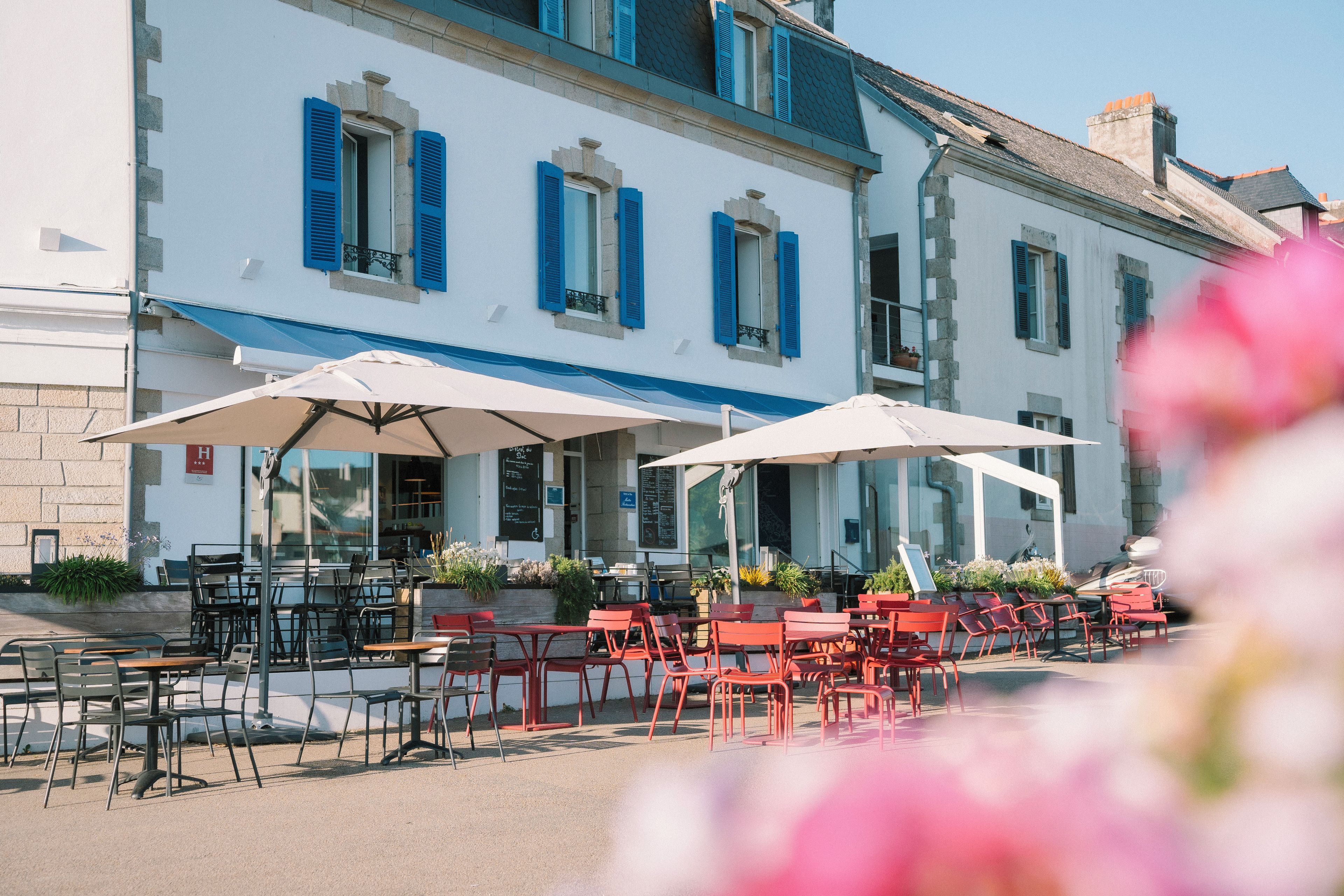 Ein Sitzbereich im Freien mit Tischen und Stühlen, ein Gebäude mit blauen Fensterläden und ein klarer Himmel.