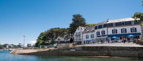 A waterfront building with a stone wall, a dock with a boat, and a clear blue sky.