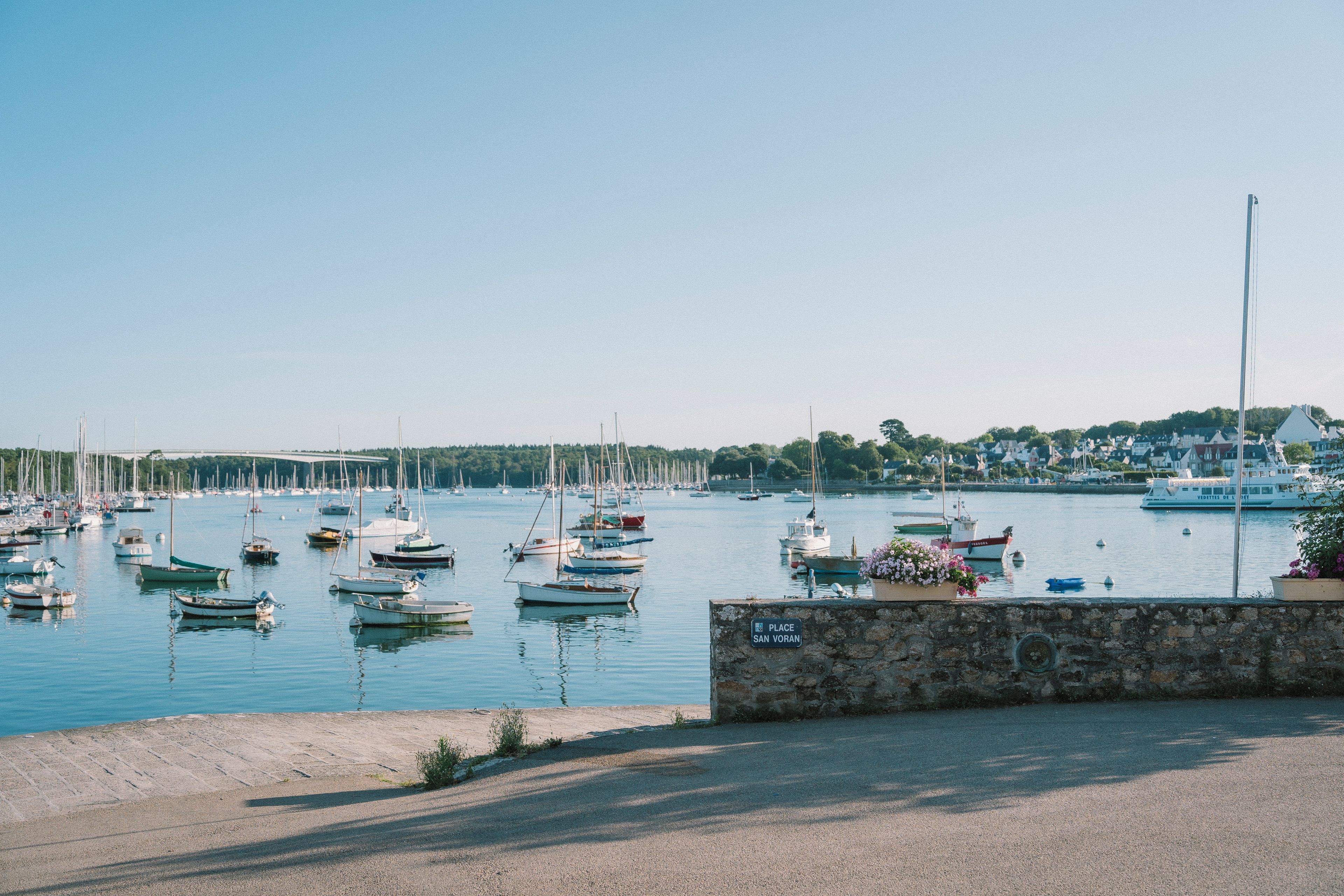 A marina with various boats docked, a stone wall, and a clear sky.