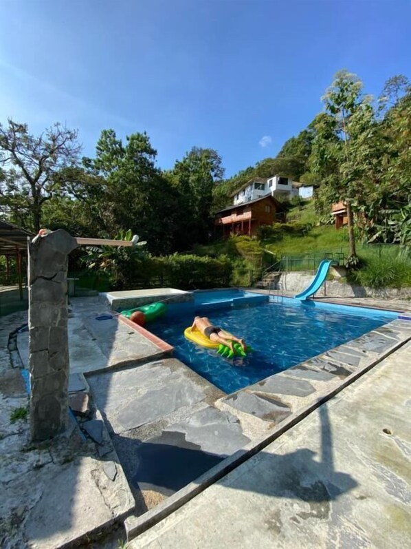 A swimming pool with a stone deck, a slide, and a person lying on a float.