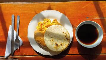 A plate with scrambled eggs, a tortilla, and a cup of coffee on a wooden table.