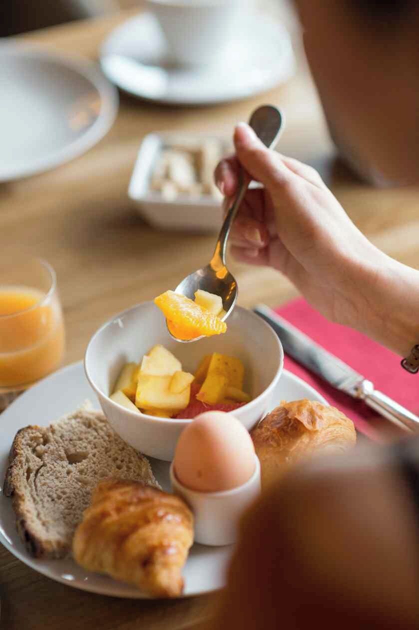 A breakfast setting with a bowl of fruit, toast, a croissant, and a glass of orange juice.