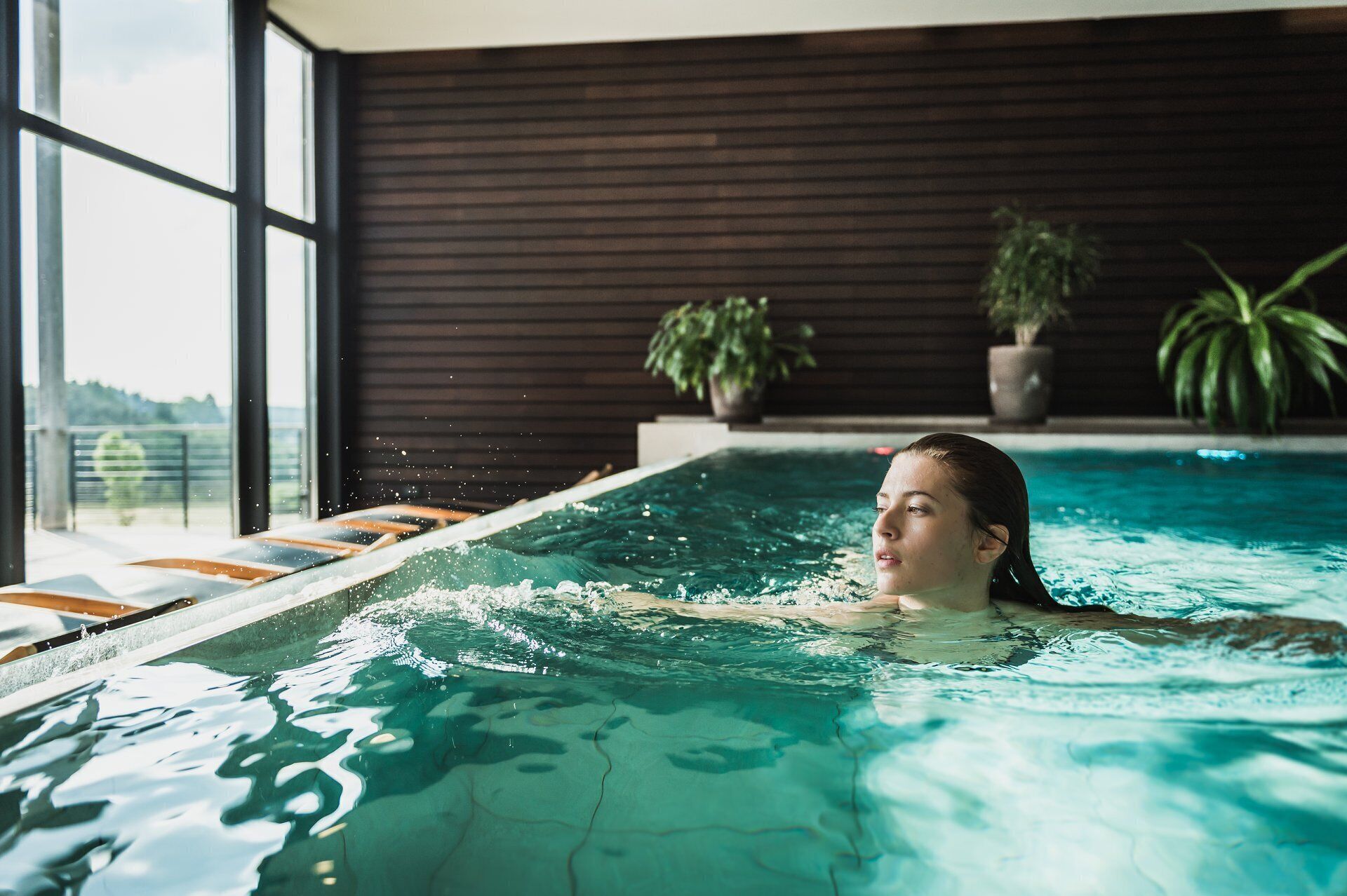 En person i en swimmingpool med udsigt til det fri via store vinduer.