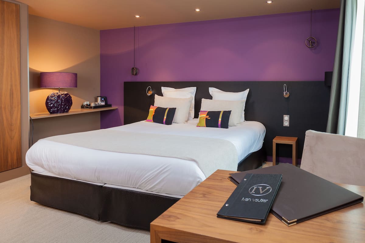 Habitación de hotel moderna con una cama grande, una mesita de noche de madera, una lámpara y vistas a la ciudad.