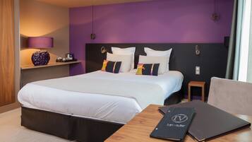 A modern hotel room with a large bed, a wooden nightstand, a lamp, and a view of the city.