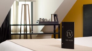 Una habitación de hotel con una cama, una mesita de noche con una tetera y una carpeta negra con la etiqueta 'IV ivan vaulter'.