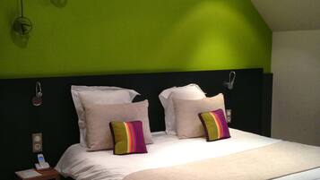 Une chambre avec un mur d’accent vert, un grand lit avec une literie blanche et des coussins colorés, une table de chevet avec un téléphone et une lampe, et une petite table de nuit.