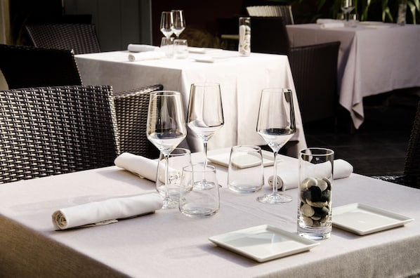 A dining table set with clear wine glasses, plates, and a glass vase with stones.