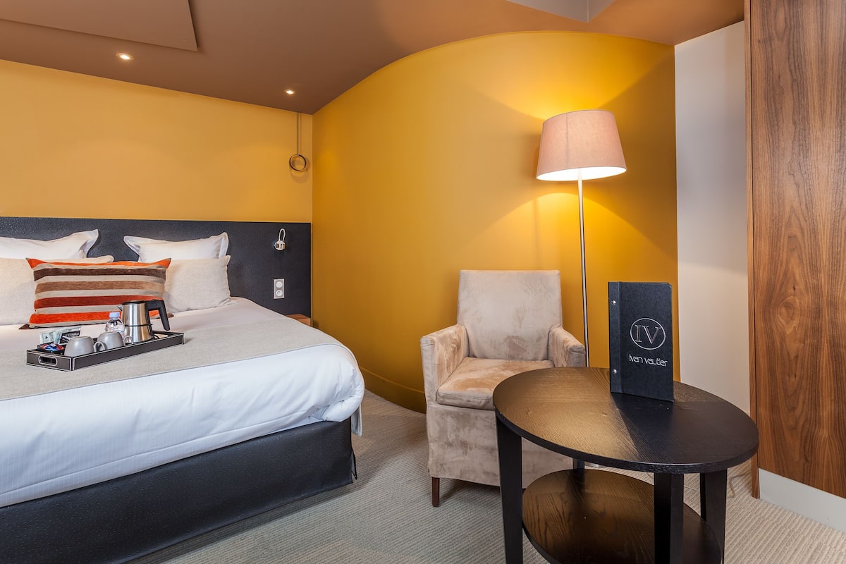 Habitación de hotel con cama, una silla, una mesa y una lámpara.