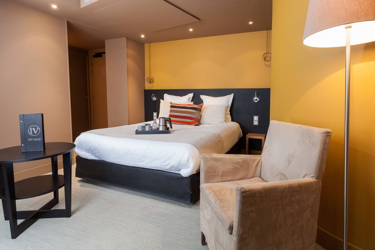 Una habitación de hotel con cama, una silla, una mesita y una lámpara.