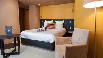 Una habitación de hotel con cama, una silla, una mesita y una lámpara.