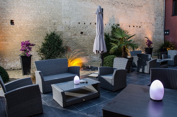 An outdoor seating area with wicker furniture, a table with a glowing light, and a stone wall in the background.