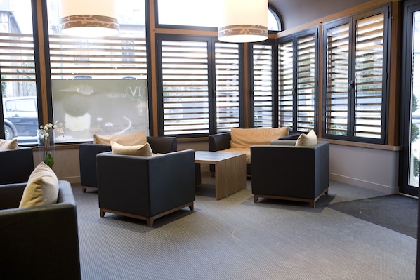 A modern lounge area with dark sofas, a wooden coffee table, and large windows with blinds. - Ivan Vautier (Caen)