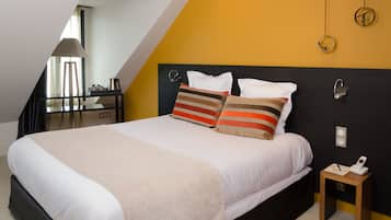 A hotel room with a bed, a bedside table, a lamp, and a small table with a phone and papers.