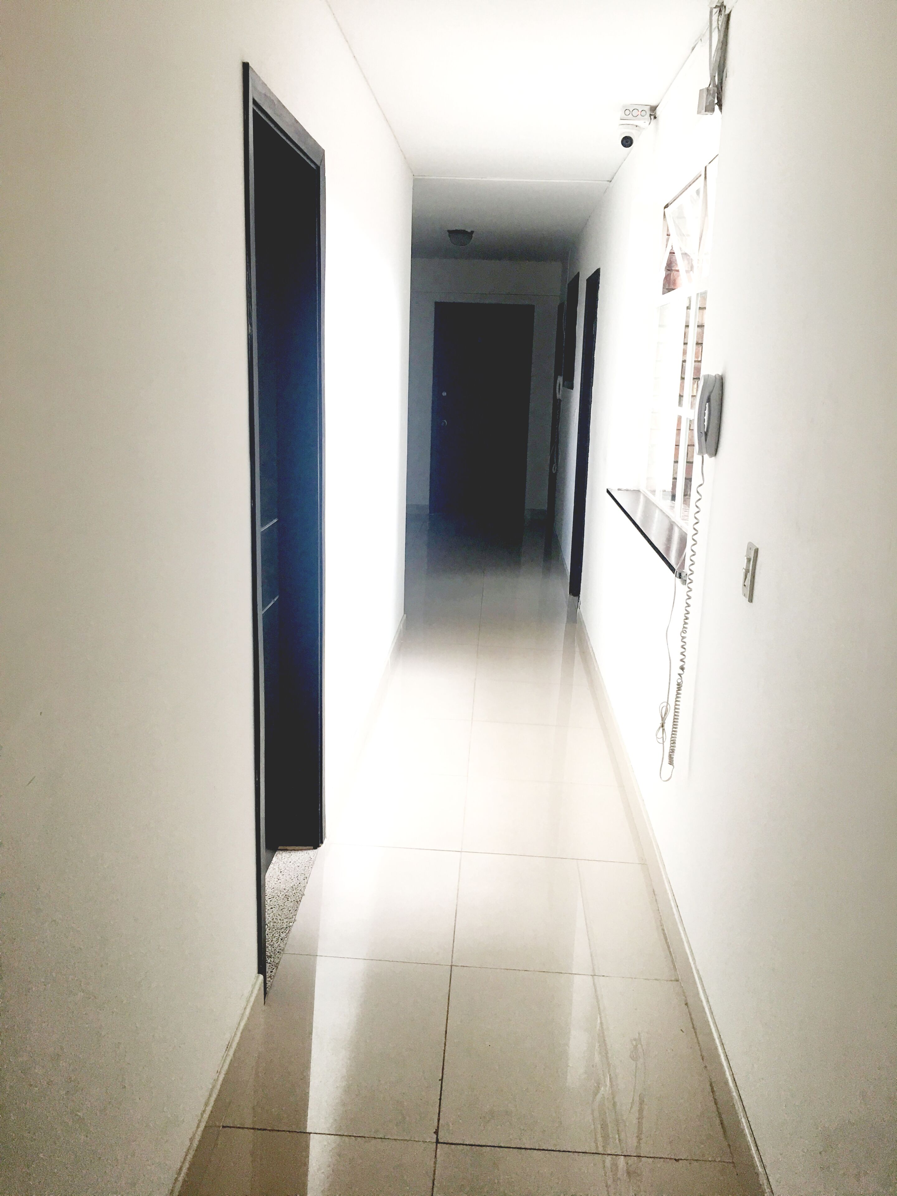 Un pasillo con paredes blancas, piso de baldosas y una puerta al final.