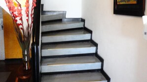 Eine Treppe mit schwarzer Geländer und weißen Stufen, die zu einer Zwischenebene mit gerahmten Kunstwerken und einem Spiegel führt.