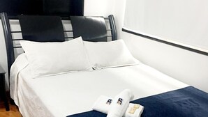 Ein ordentlich bezogenes Bett mit weißen Laken und einer dunkelblauen Decke, ein schwarzes Kopfteil und ein Holzboden.