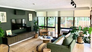 Ein modernes Wohnzimmer mit Flachbildfernseher, grünem Sofa und großen Fenstern.