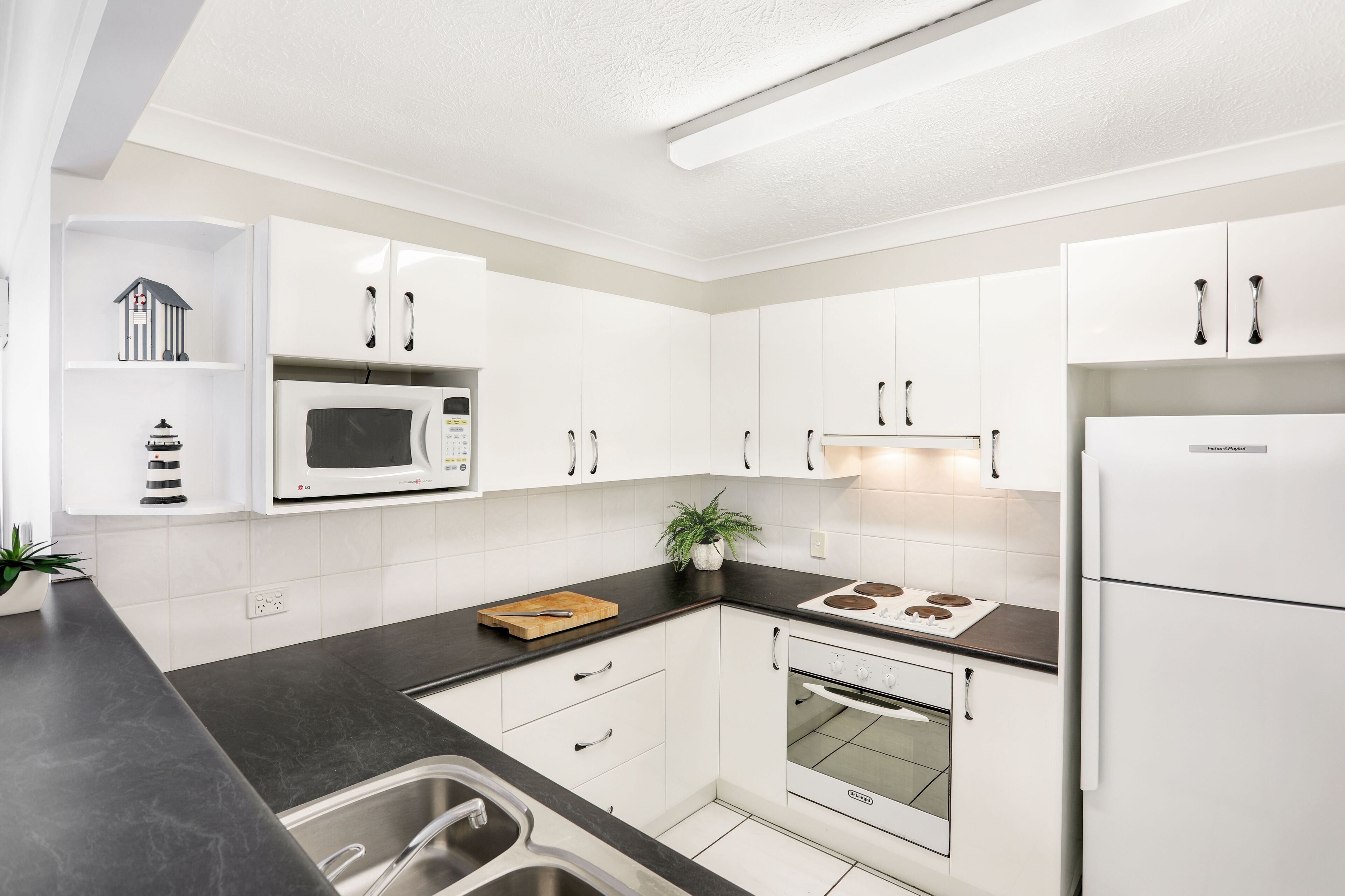 A modern kitchen with white cabinets, a microwave, stove, and a refrigerator.
