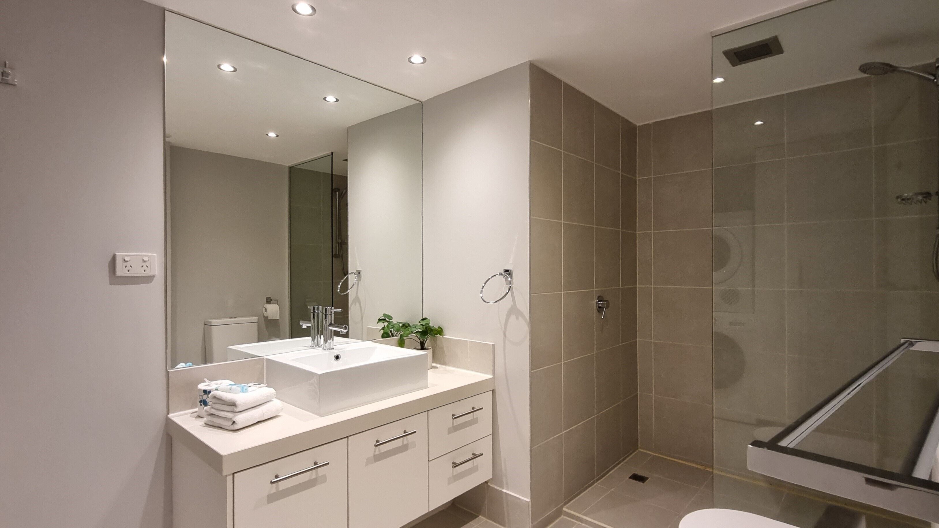 Une salle de bain moderne avec un grand miroir, un lavabo blanc et une douche à parois de verre.