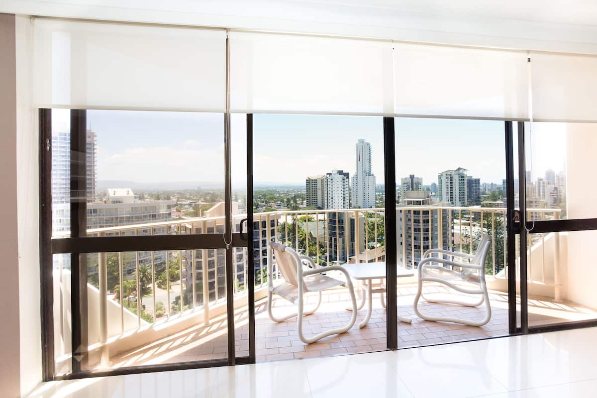 A balcony with a view of a cityscape, featuring a white chair and a table.