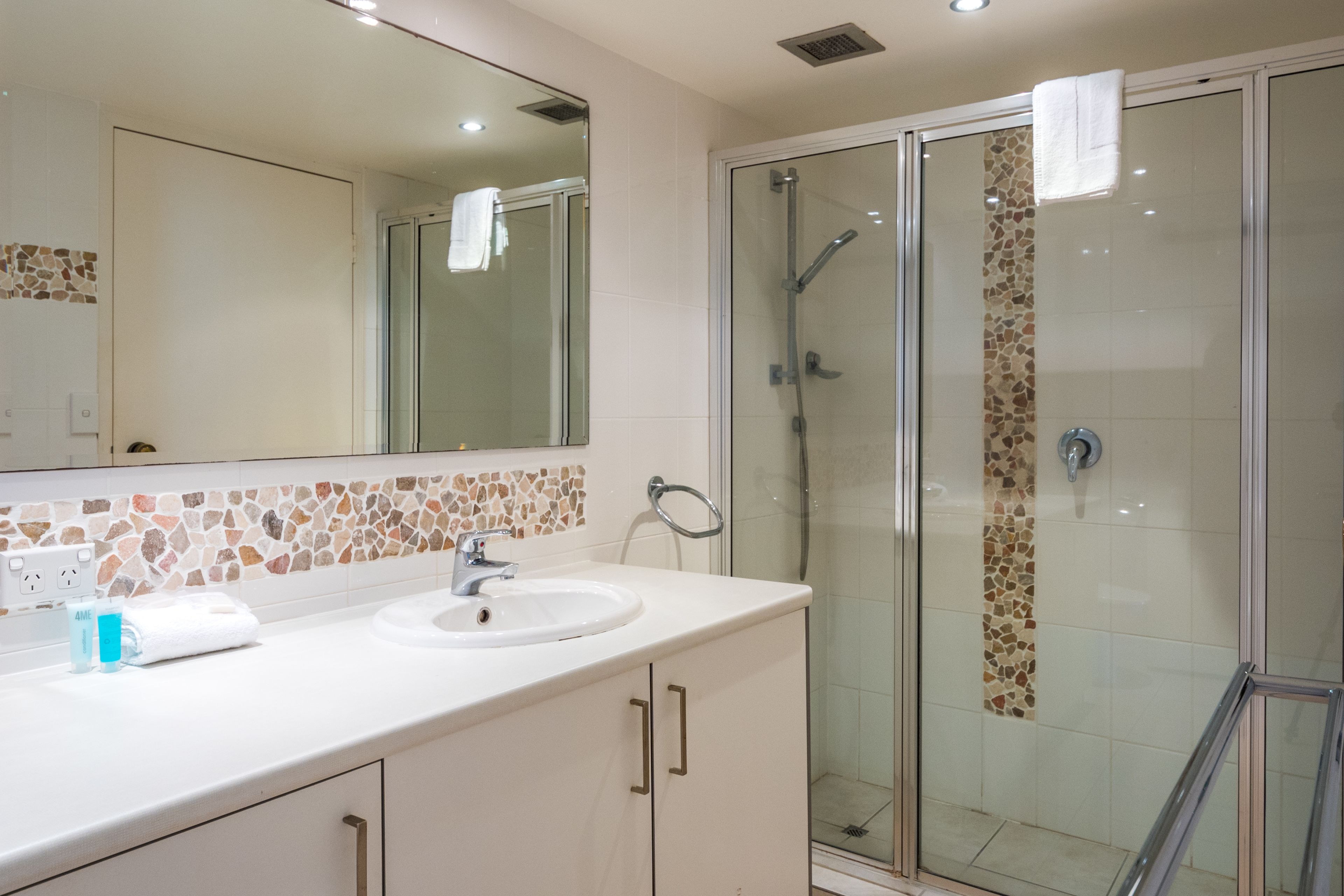 A bathroom with a glass-enclosed shower, a sink with a mirror above it, and a tiled backsplash.