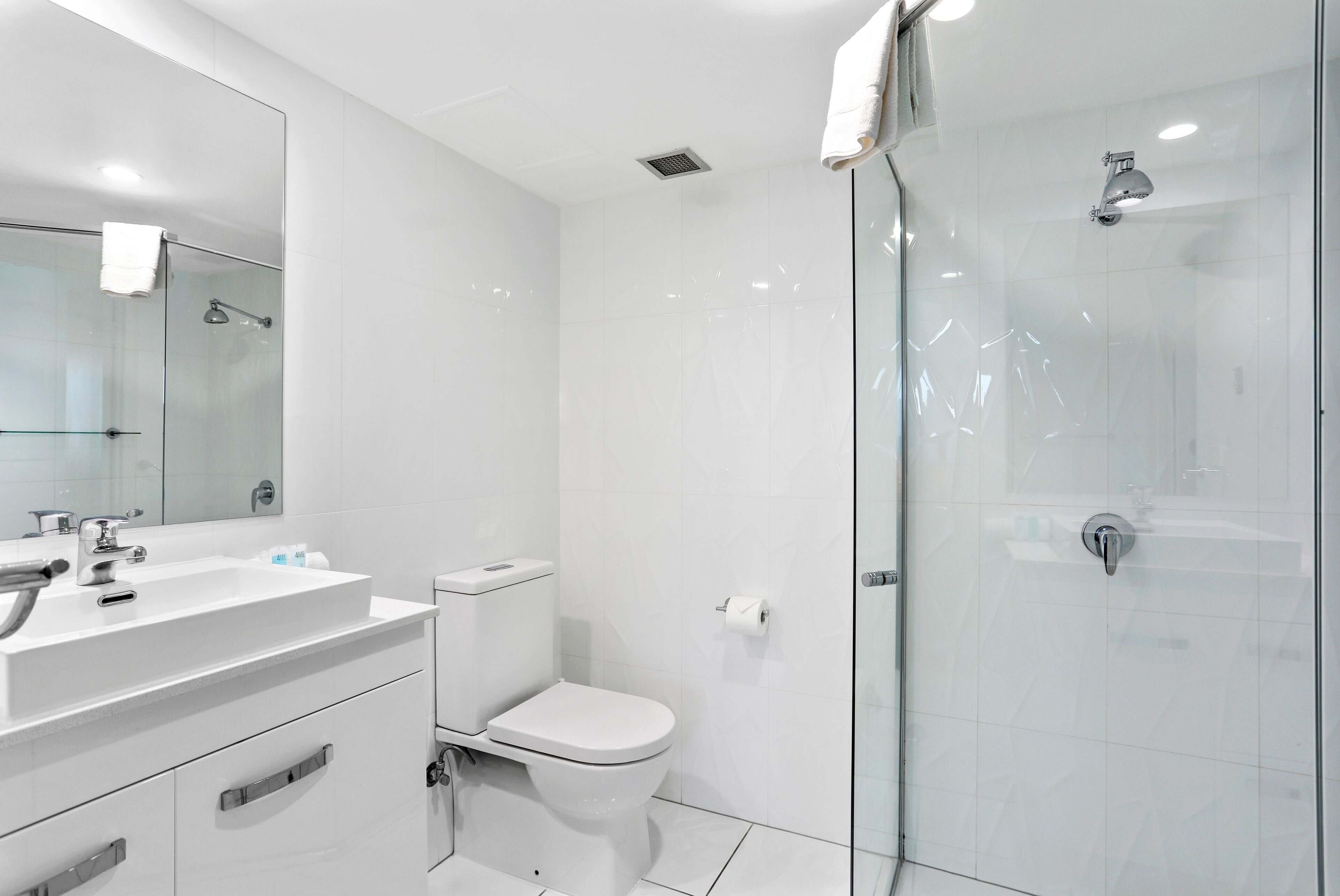 Un bany modern amb un espai de dutxa de vidre, un lavabo blanc i un vàter.