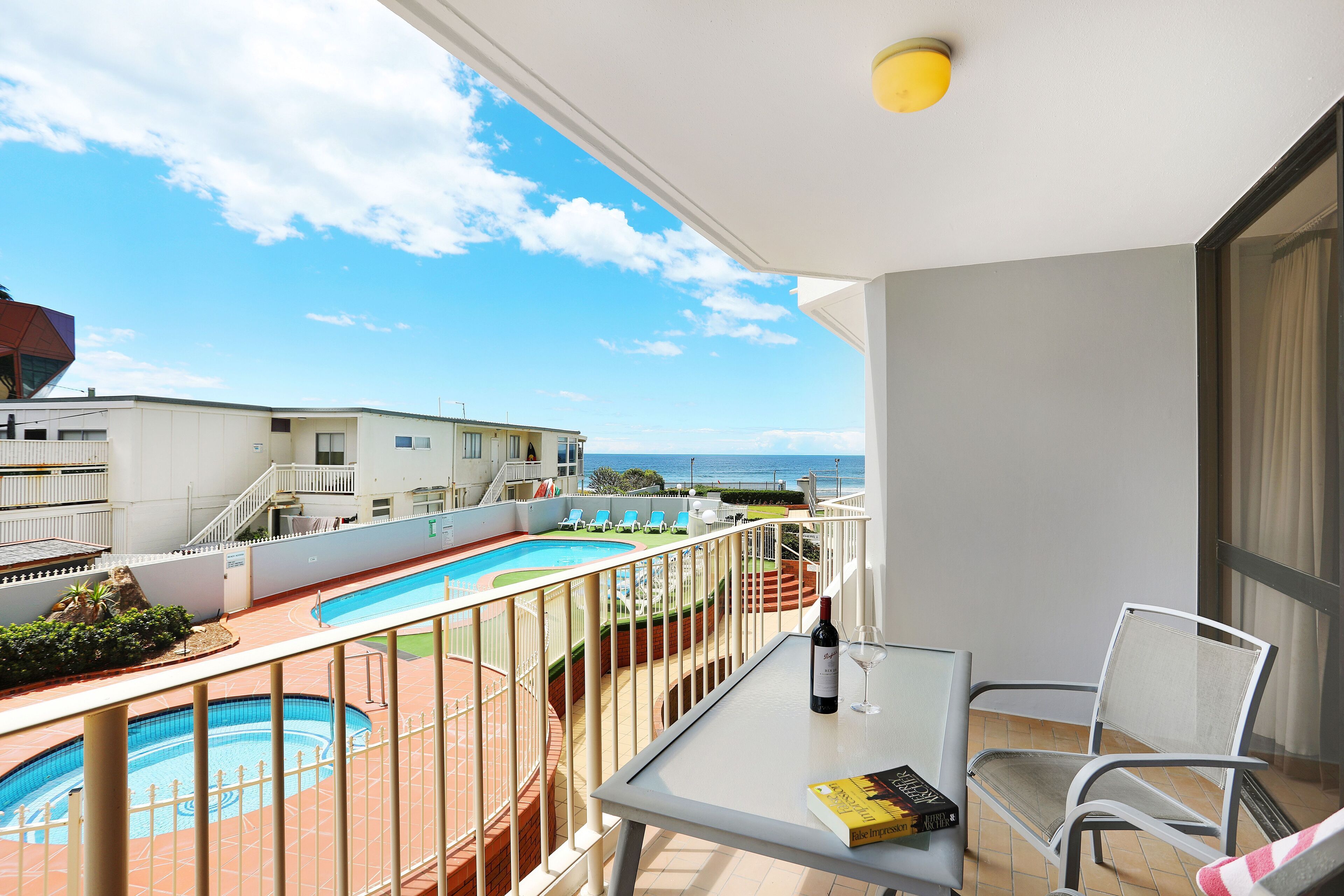 A balcony with a pool, a table with a bottle and a book, and a chair.