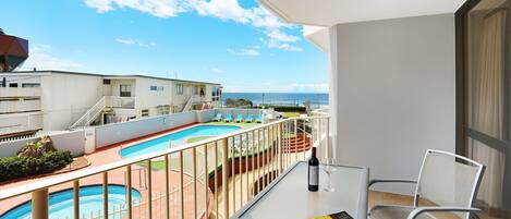 Un balcon avec une piscine, une table avec une bouteille et un livre, et une chaise.