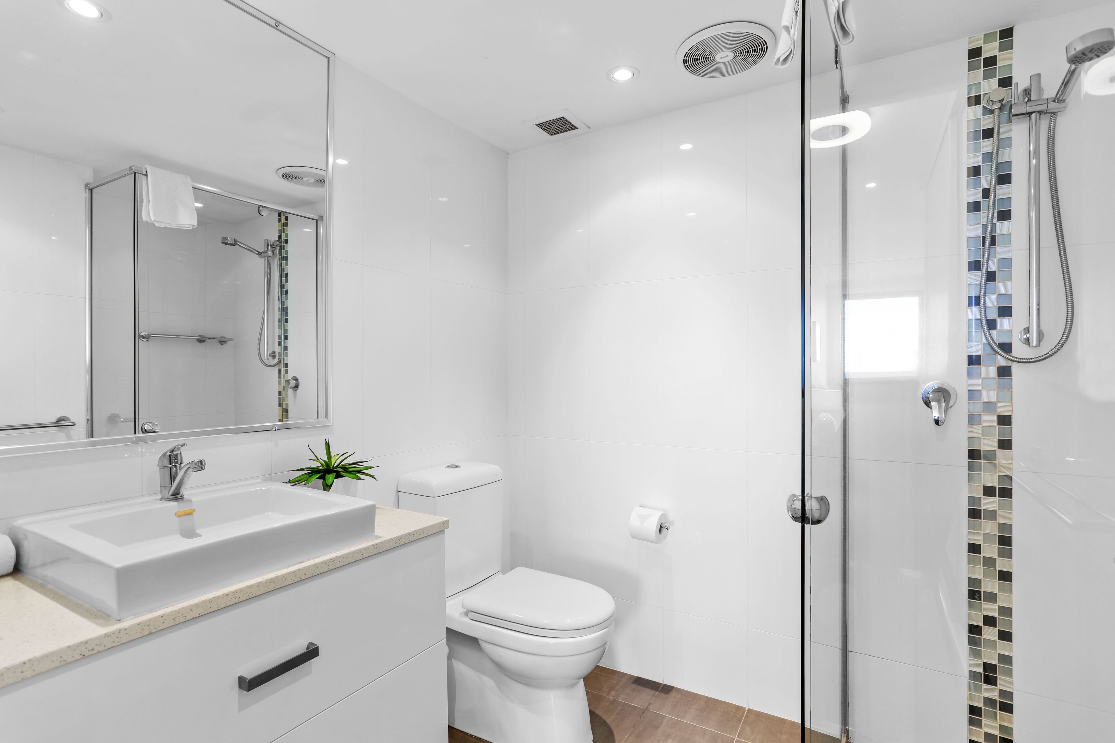 Een moderne badkamer met een douchecabine van glas, een witte wastafel en een toilet.