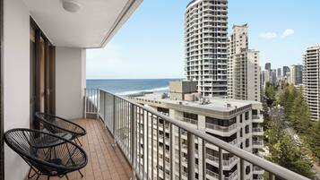 A balcony with two chairs, a view of the ocean, and high-rise buildings in the background.
