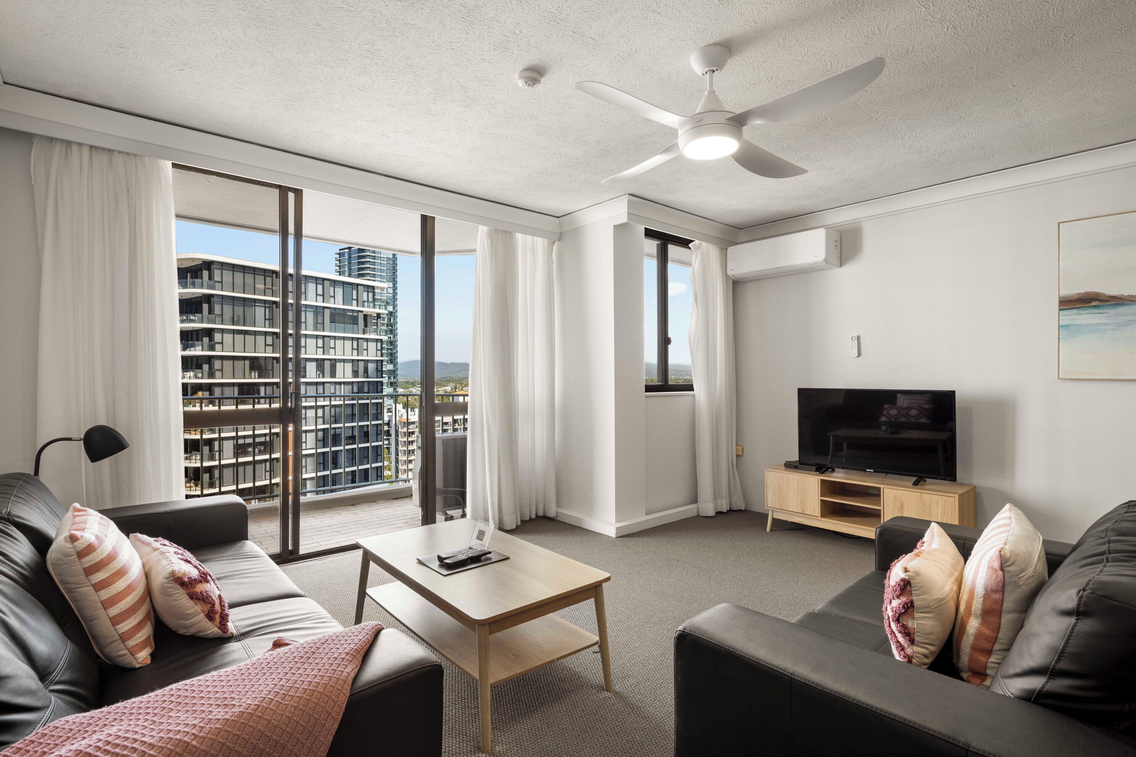 Ein modernes Hotelzimmer mit Sofa, Couchtisch, Fernseher und einem Balkon mit Blick auf die Stadt.