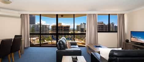 Habitación de hotel moderna con un balcón grande, televisor de pantalla plana y un área de estar con sofá y sillones.