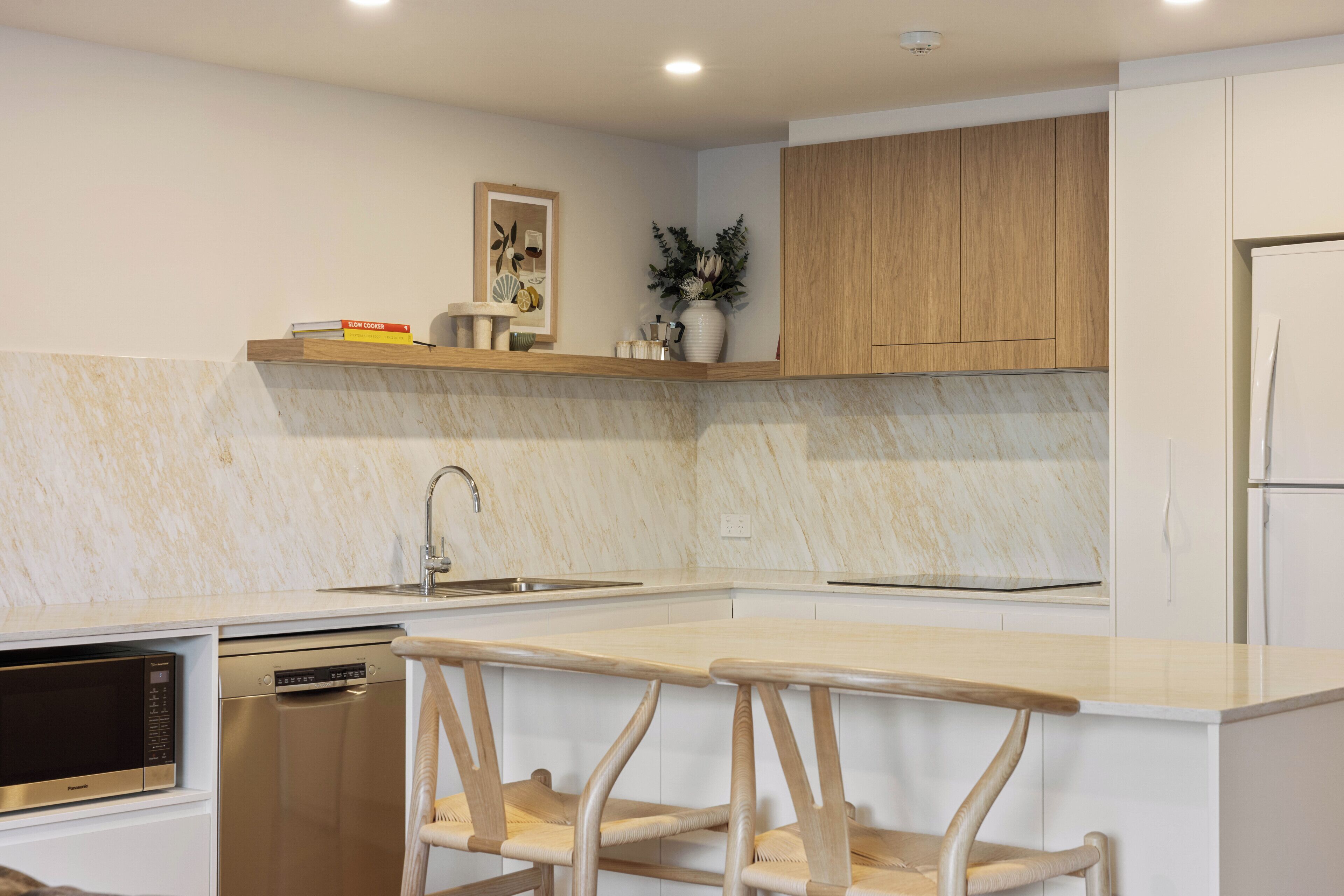 Een moderne keuken met vaatwasser, magnetron, houten kastjes en een marmeren aanrecht.