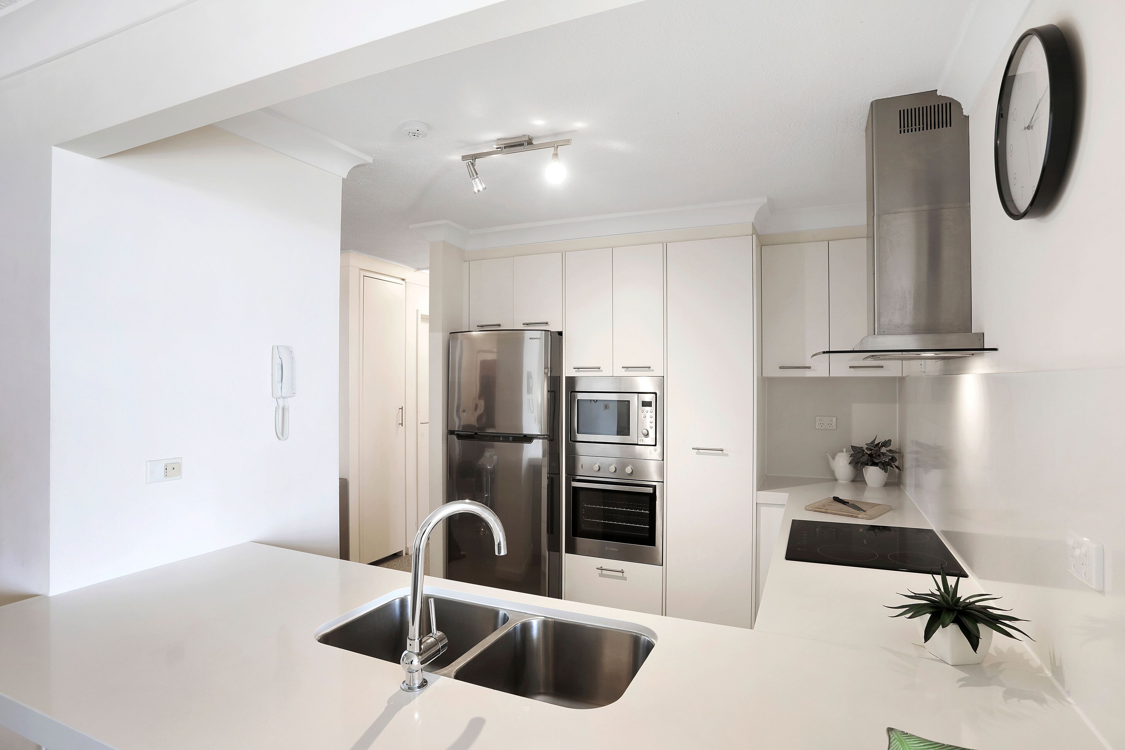 Una cocina moderna con electrodomésticos de acero inoxidable, un lavamanos y un reloj en la pared.