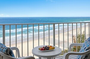 Un balcón con una mesa blanca y dos sillas, con vista a la playa y al océano.
