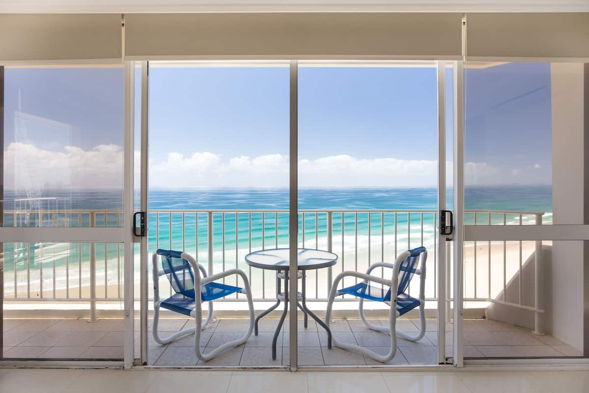 A balcony with a glass door, two blue chairs, and a small table.