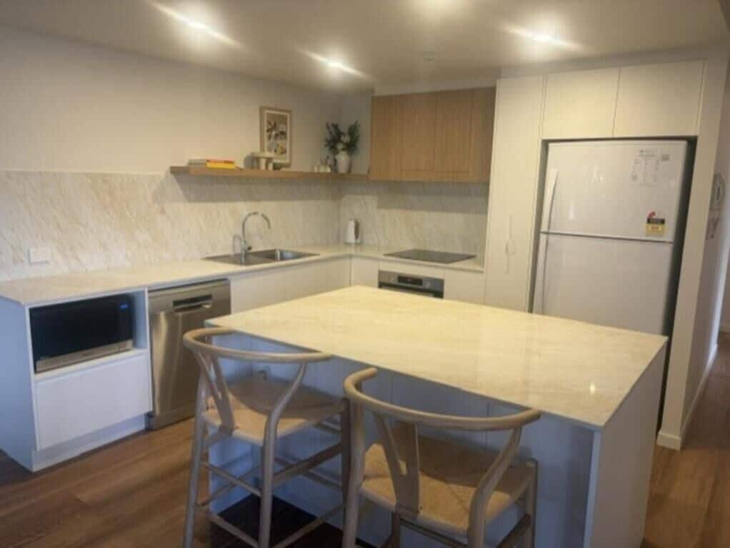 Een moderne keuken met een centraal kookeiland, barstoelen, een vaatwasser en een koelkast.