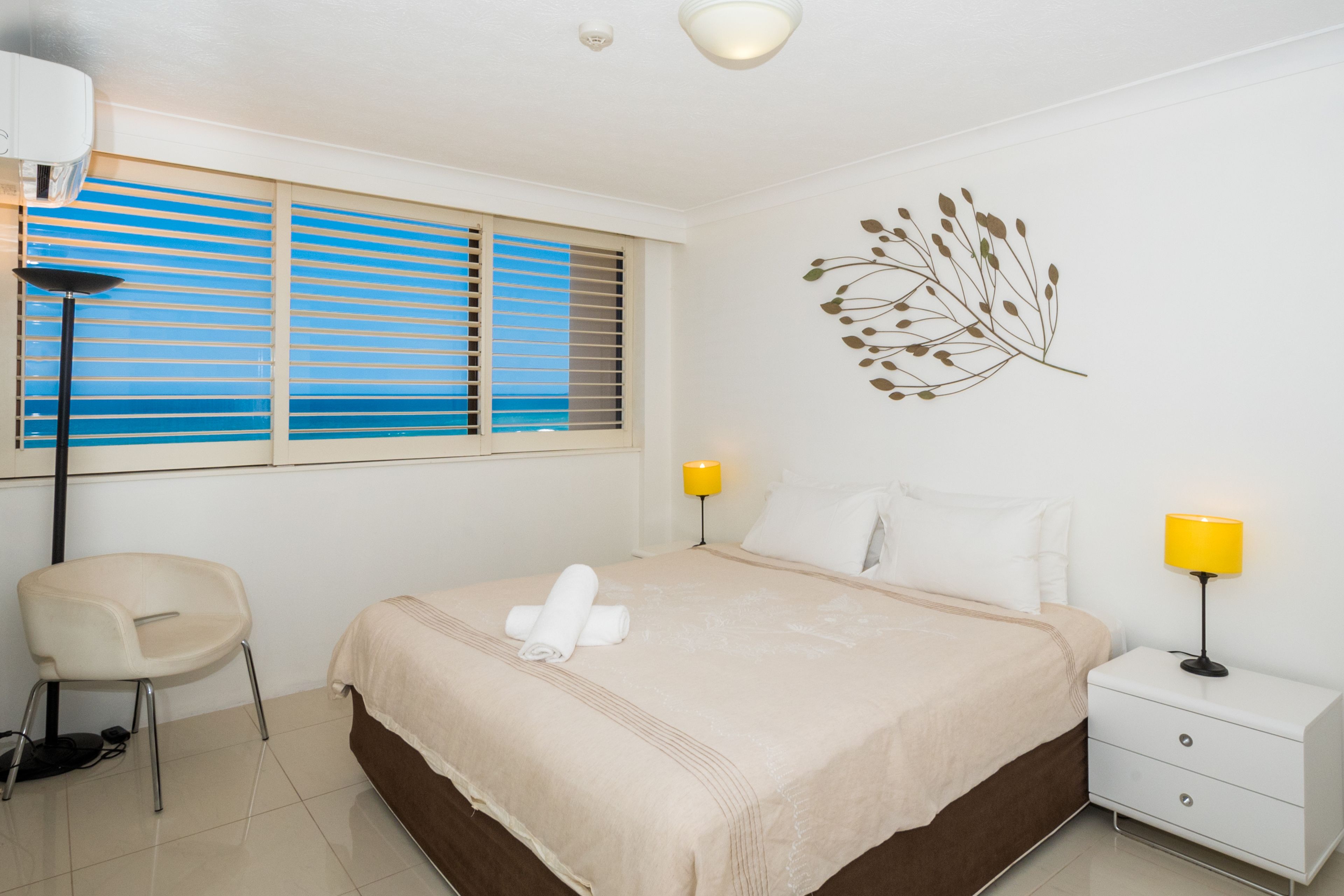 A neatly arranged bedroom with a bed, bedside lamps, a chair, and a window with blinds.