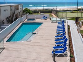 Una piscina en la azotea con agua cristalina azul, rodeada de sillones azules y vista al océano.