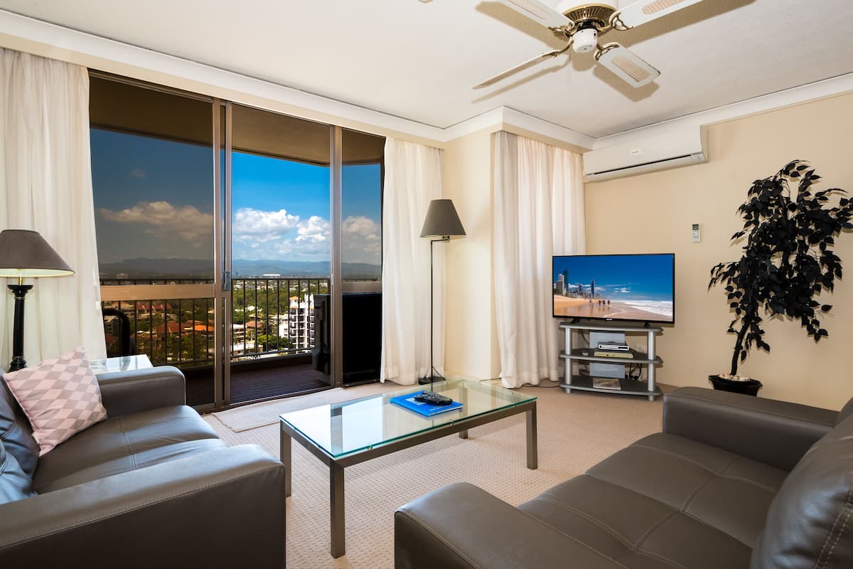A modern hotel room with a balcony, a flat-screen TV, leather sofas, and a glass coffee table.