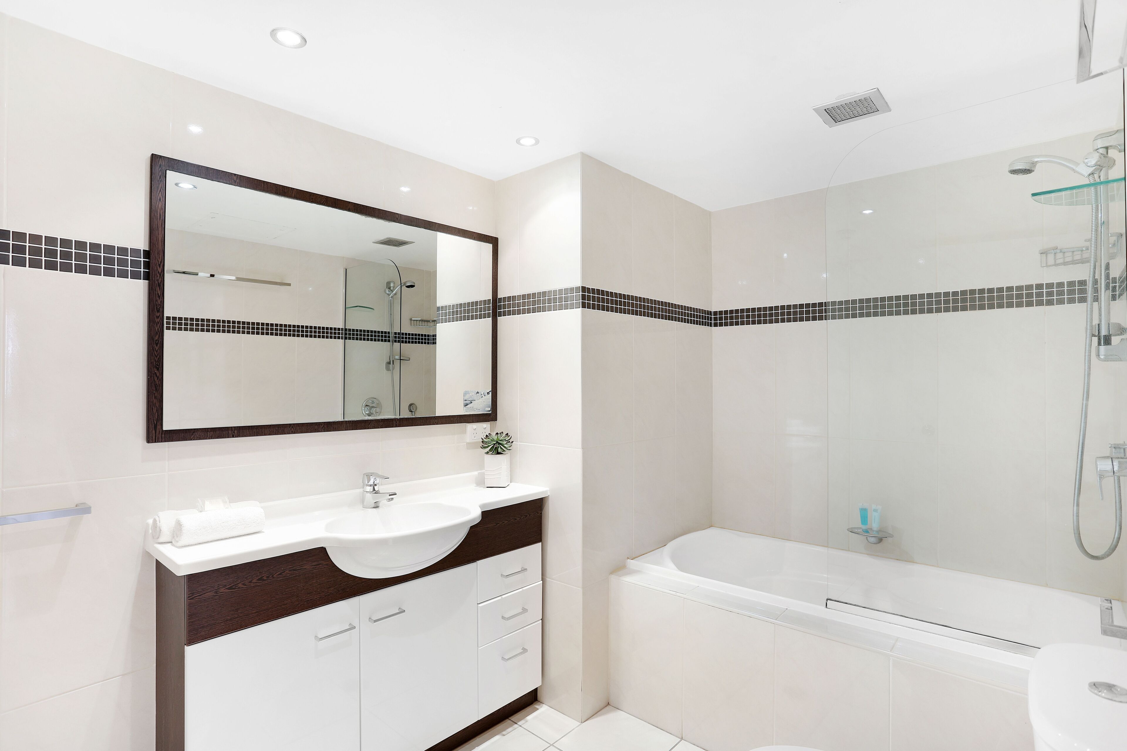 Une salle de bain moderne avec un grand miroir, un lavabo blanc, un meuble-lavabo en bois foncé, une douche à parois de verre et une baignoire blanche.