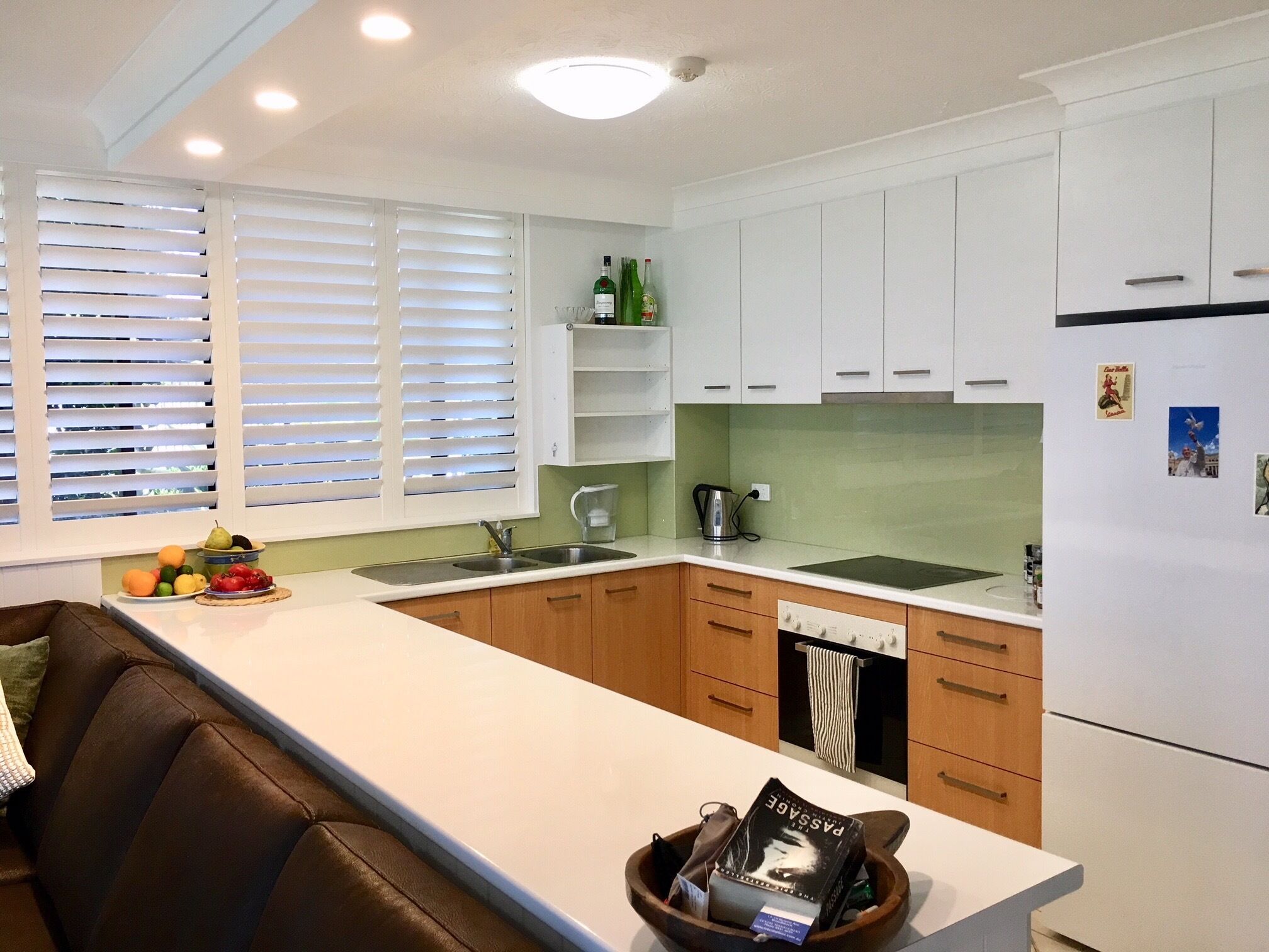 Una cocina moderna con armarios blancos, una isla central y un comedor con sofá de cuero marrón.