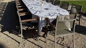 Un espacio exterior para comer con una mesa larga, sillas y un edificio de piedra al fondo.