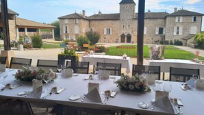 Un espacio de comedor al aire libre con mesas dispuestas para una comida, con vistas a un edificio histórico de piedra con torre.