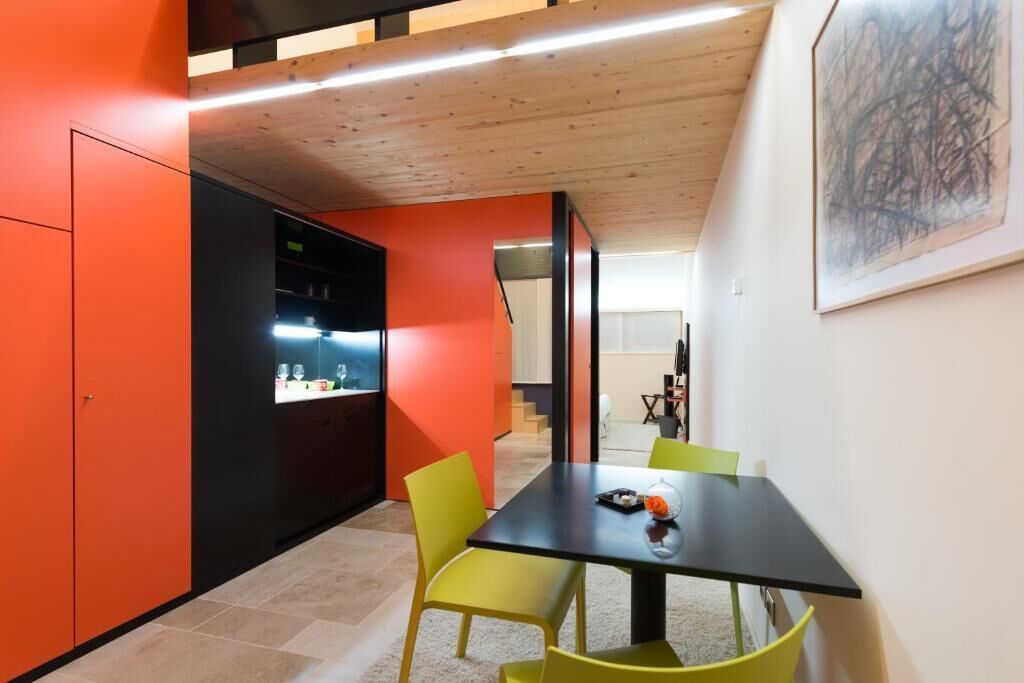 A modern kitchen with orange cabinetry, a black countertop, and a dining area with a black table and yellow chairs.