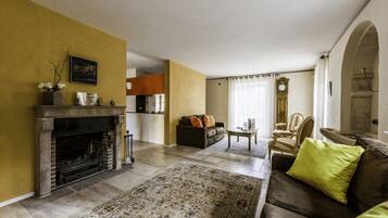 Un salon avec une cheminée, un canapé, une table basse et, au fond, un coin repas.
