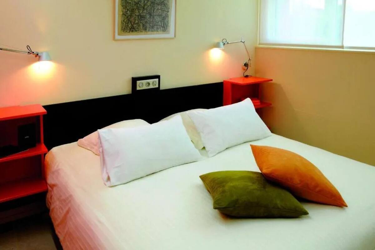 A hotel room with a bed, two bedside tables, two lamps, a window, and a painting on the wall.